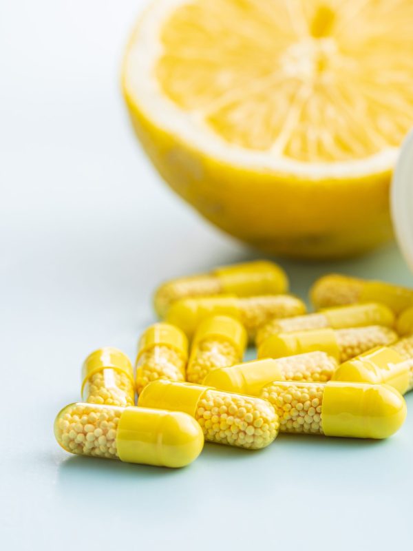 Vitamin capsules. Vitamin C pills, lemon fruit and pill bottle on blue background.